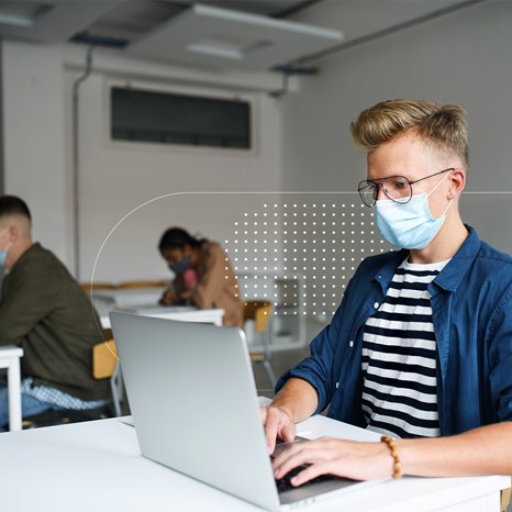 Man typing, wearing mask, posing for photo