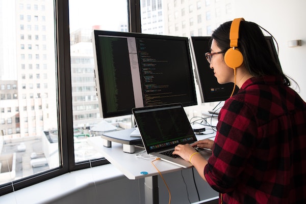 Woman wearing headset, viewing laptop screen, typing and coding