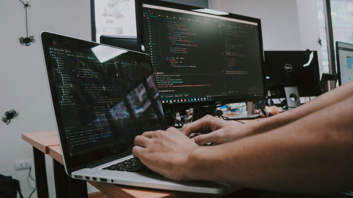 A man viewing a laptop screen, typing, and coding