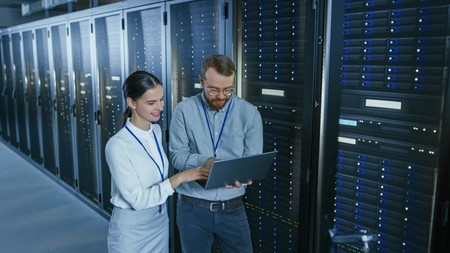 Man and woman checking in laptop, background server room