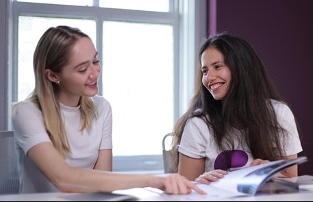 Two Women smiling, showing in the booklet, posing for photo