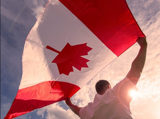 
Man holding canadian flag, standing at sunrise, posing for photo