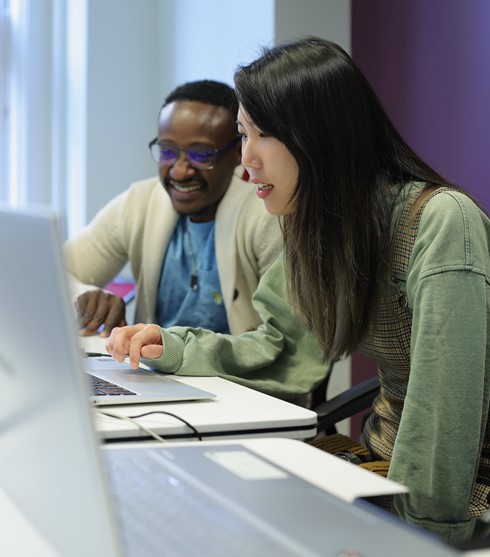 Woman smiling, typing, man smiling, watching the screen posing for photo
