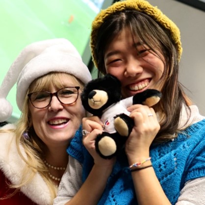 Two Women smiling, holding teddy, posing for photo