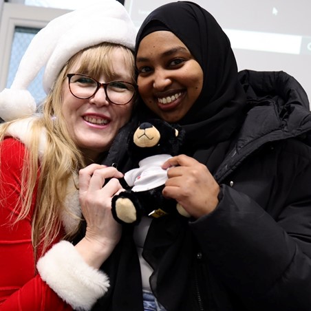 Two Women smiling, holding teddy, posing for photo