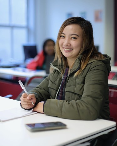 Woman smiling, holding pen, posing for photo