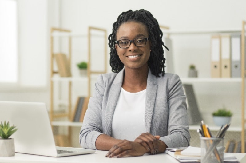 Woman smiling, wearing glasses, posing for a photo with a laptop