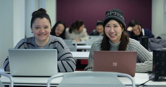 Two women smiling, typing, posing for a photo