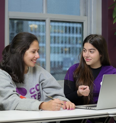 Two women discussing, one is noting with pen, posing for photo