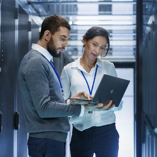 Man and Woman checking in laptop, background server room, posing for photo