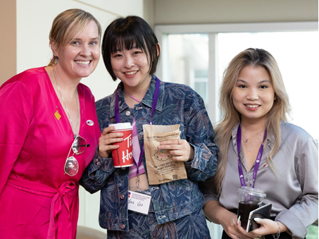 Three women smiling, holding coke, posing for photo