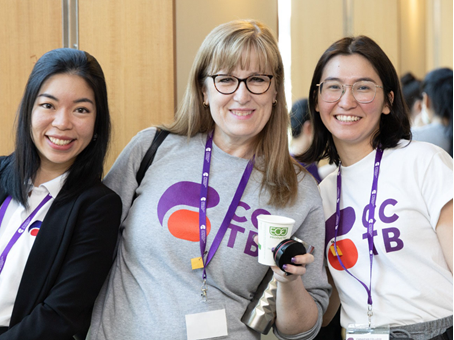 Three women smiling, wearing ID card, posing for photo