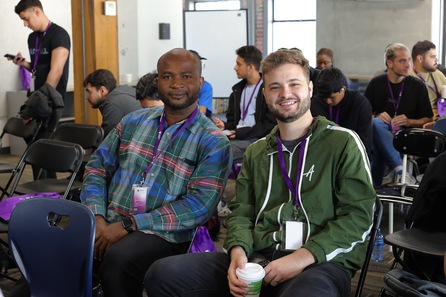 Two men sitting, wearing ID card, posing for photo
