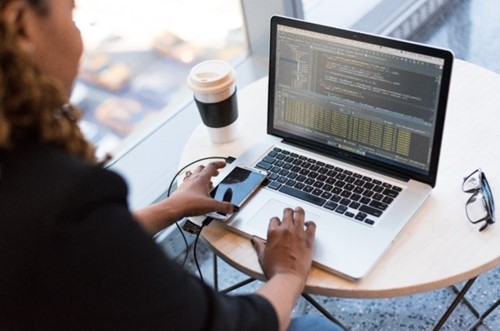 Woman viewing laptop screen, holding mobile and typing