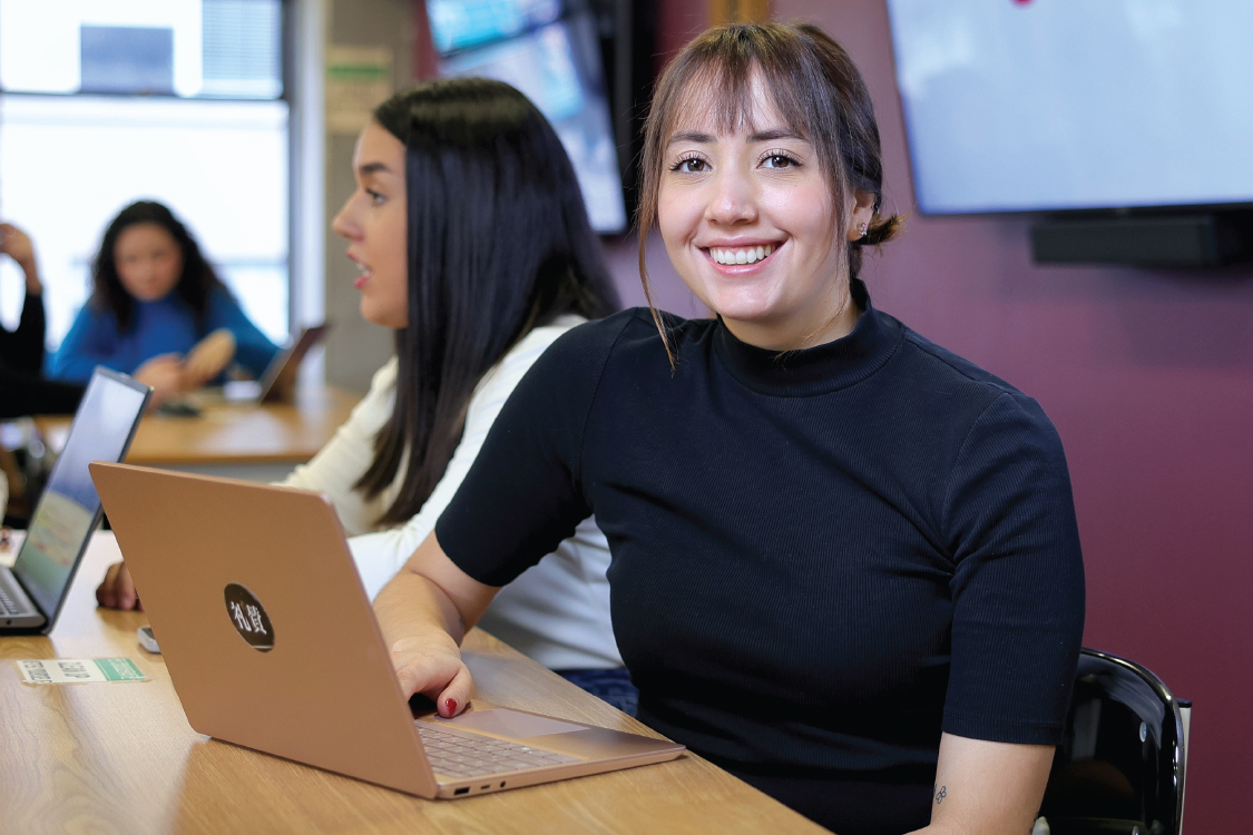A smiling student using a laptop and looking at the camera