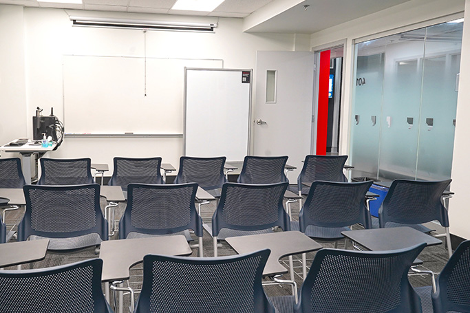 Empty classroom with rows of chairs facing a whiteboard and projector screen